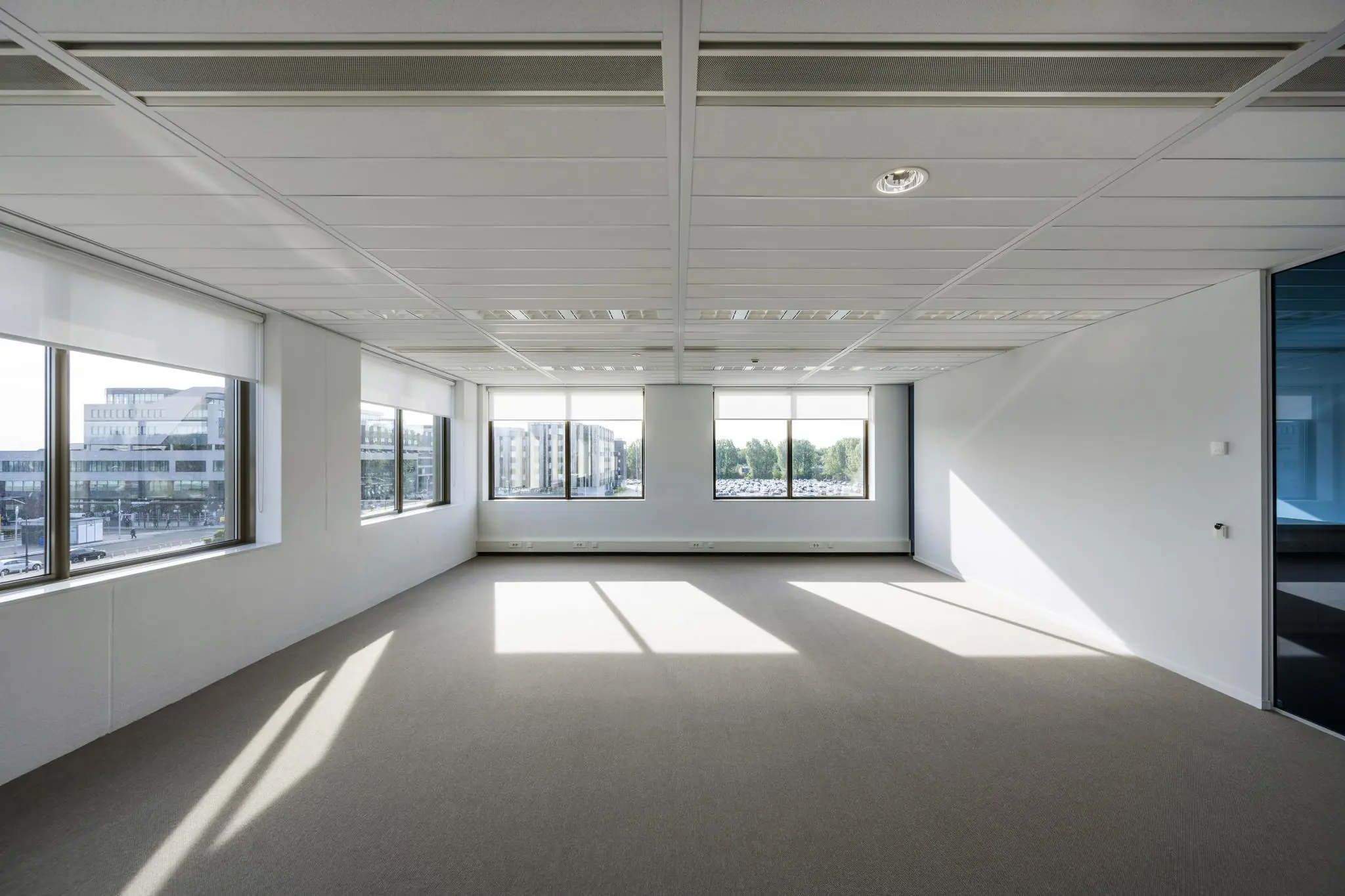 Licht en leeg kantoorpand met uitzicht op Rotterdam Airportplein door grote ramen.